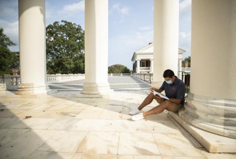 A masked student studies on the porch of the UVA Rotunda