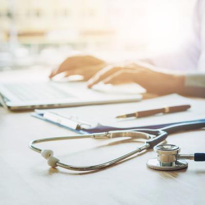 Stethoscope in foreground, doctor on laptop in background